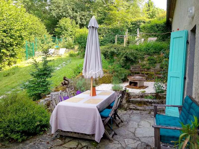 La table de jardin dressée sous le parasol, sur la terrasse en pierre
